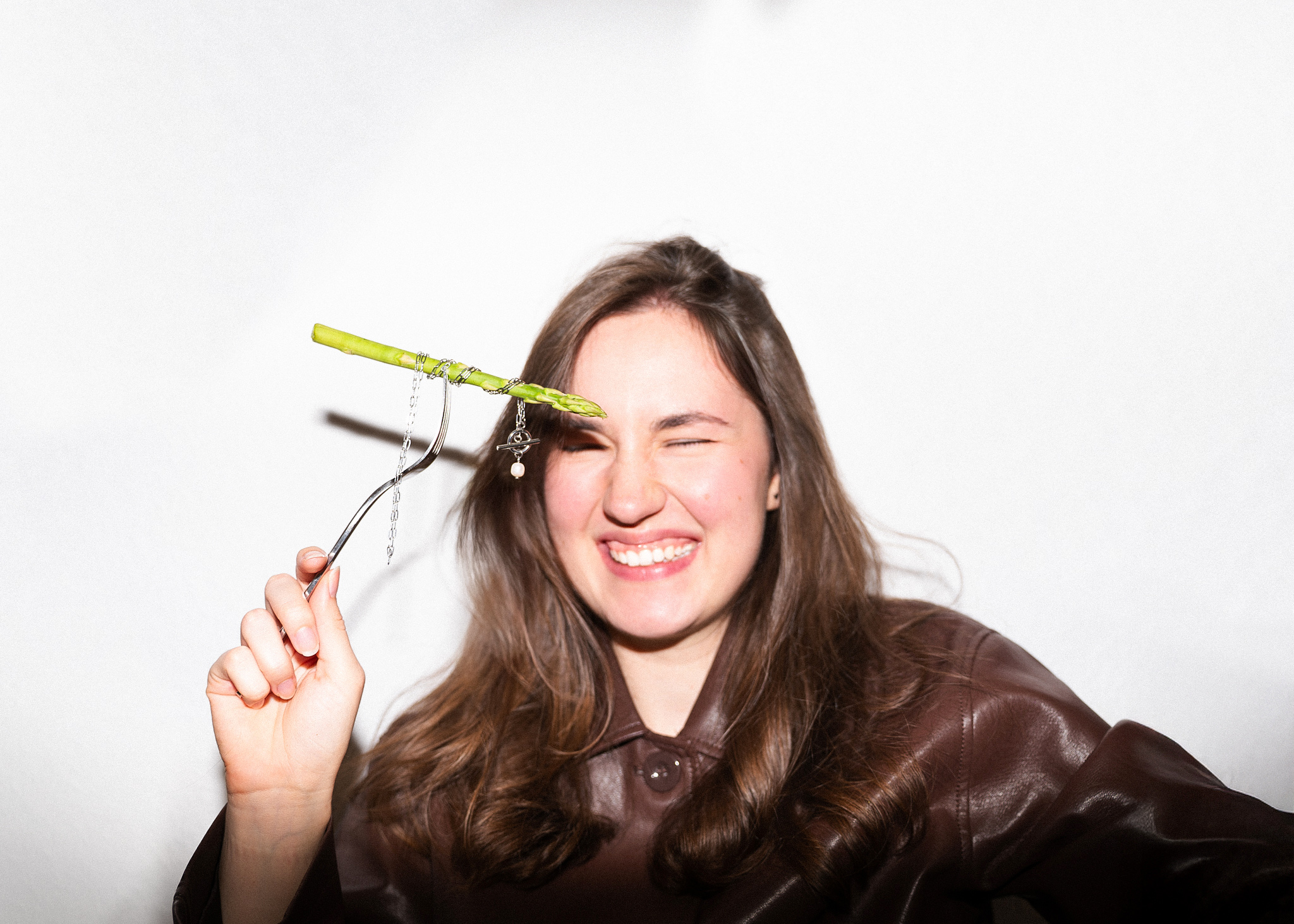 a woman is laughing while holding a fork with jewellery and aspargues on it