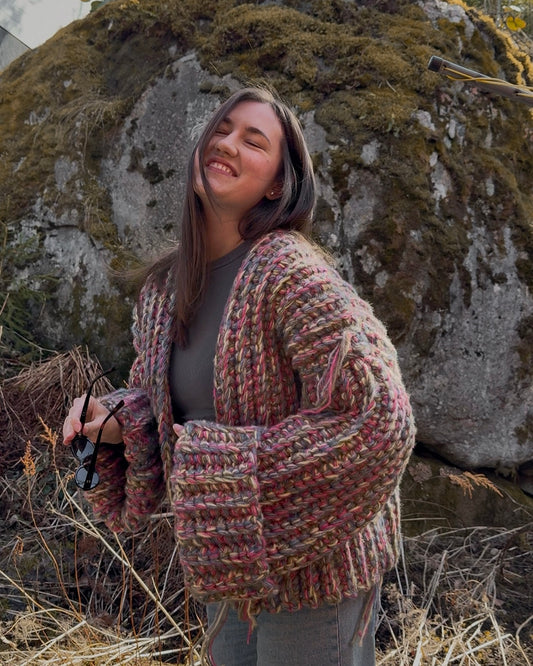 Woman wearing a patterned cardigan standing in front of a large stone wall with moss.
