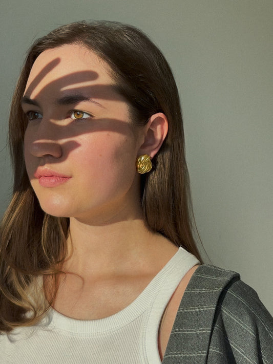 Woman wearing sculptural gold earring in sunlight with shadow play.  Retro. Vintage. Chunky earrings. Hand-made.