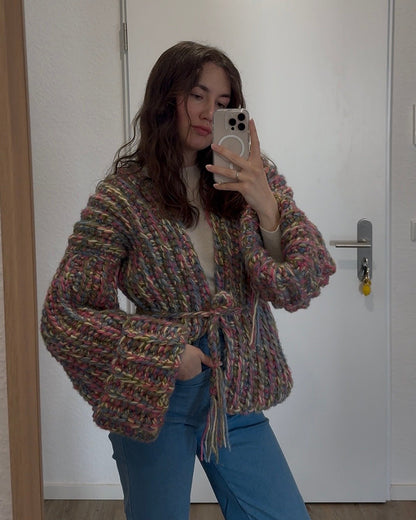 Person wearing a patterned jacket and blue jeans taking a mirror selfie.