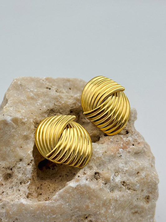 Goldene Edelstahl-Ohrringe mit überkreuztem Rillen-Design, auf hellem Naturstein platziert.