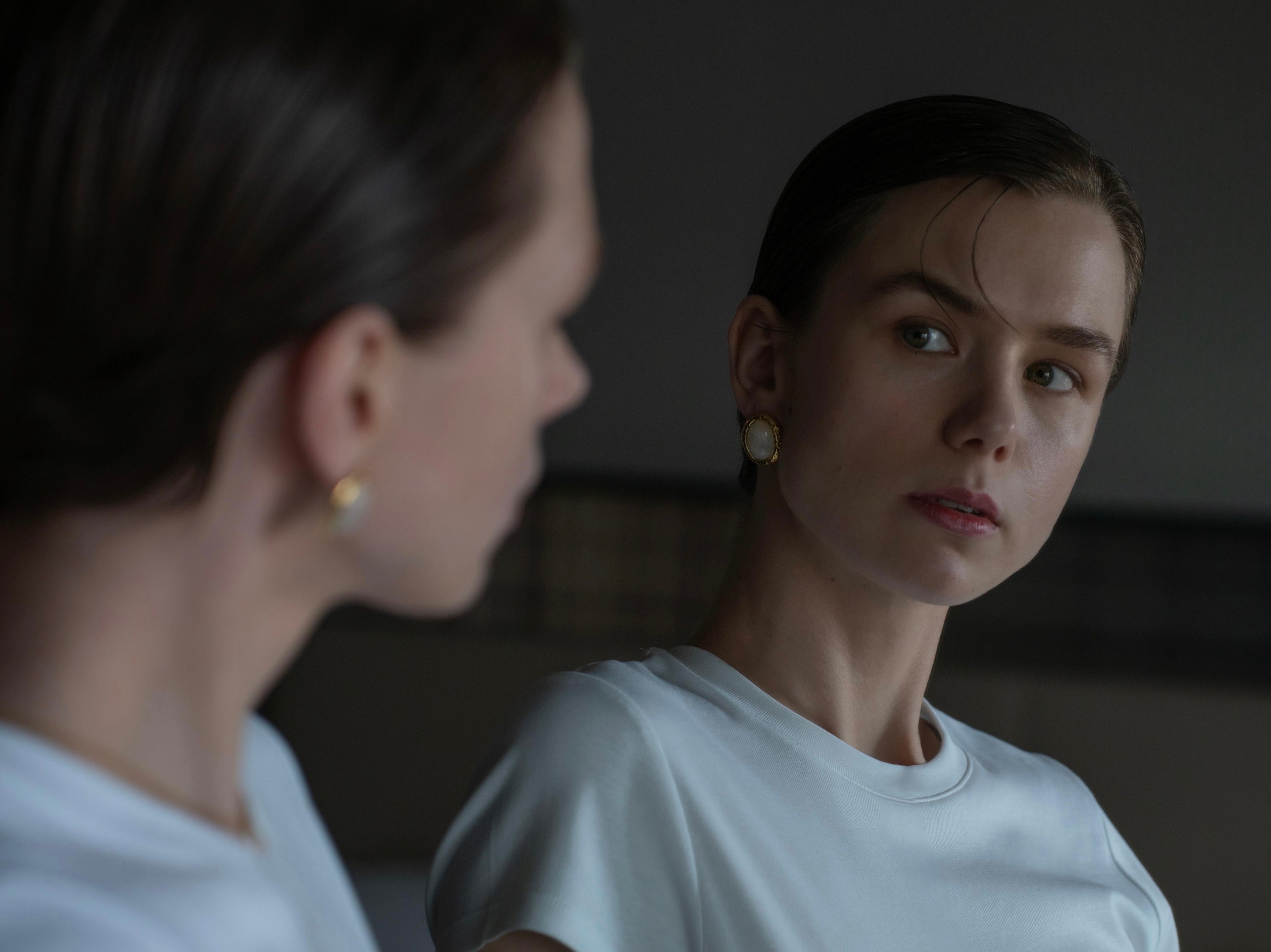 a young woman wearing white vintage earrings looking at herself into the mirror