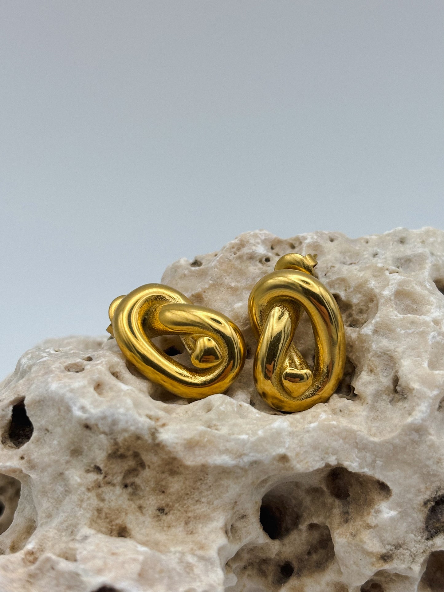 Gold abstract knot stud earrings with sculptural twist design, displayed on porous natural stone — modern artistic jewelry with a minimalist edge