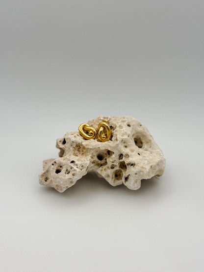 Gold abstract knot stud earrings with sculptural twist design, displayed on porous natural stone — modern artistic jewelry with a minimalist edge