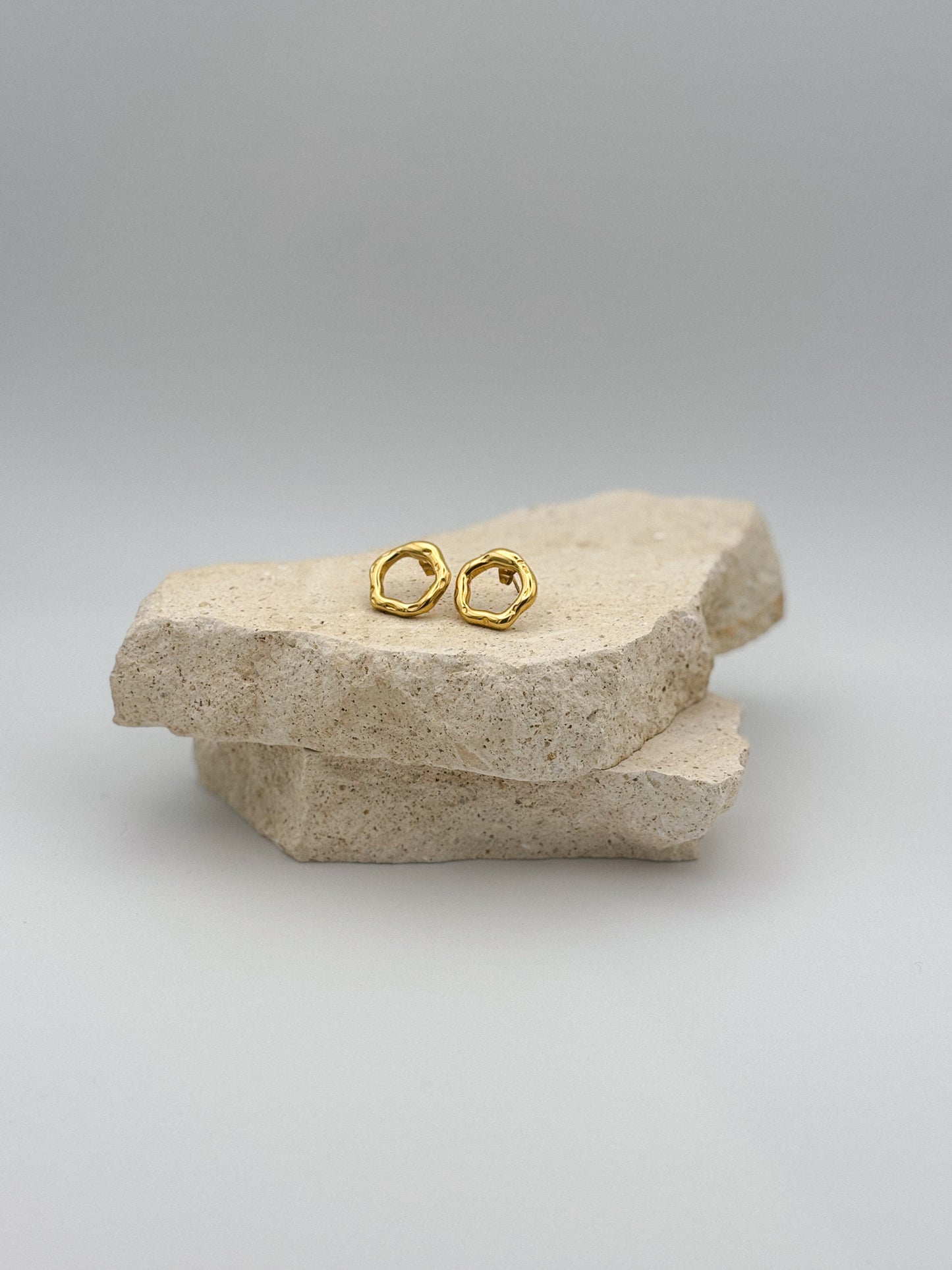 Minimalist gold stud earrings with organic, irregular shape displayed on natural stone slabs — modern and elegant jewelry for everyday wear