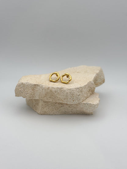 Minimalist gold stud earrings with organic, irregular shape displayed on natural stone slabs — modern and elegant jewelry for everyday wear
