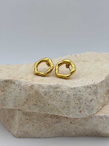 Gold open circle stud earrings with hammered organic texture, displayed on natural stone — artistic minimalist design, modern and timeless jewelry