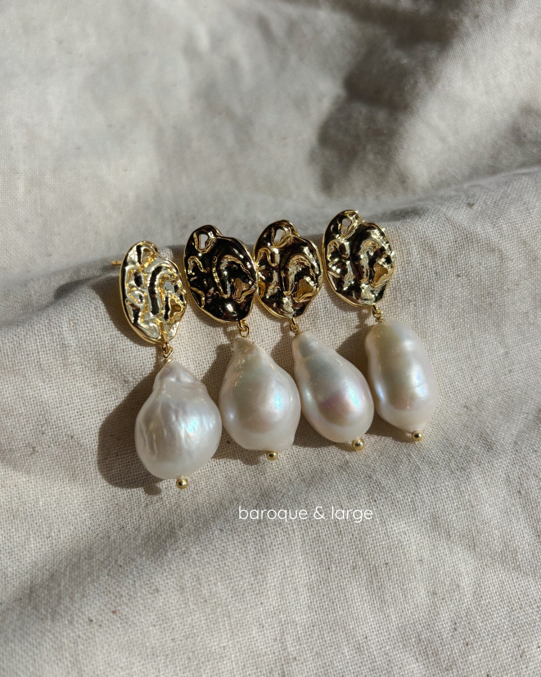 four baroque pearl earrings are laying on a beige textile under soft sunlight