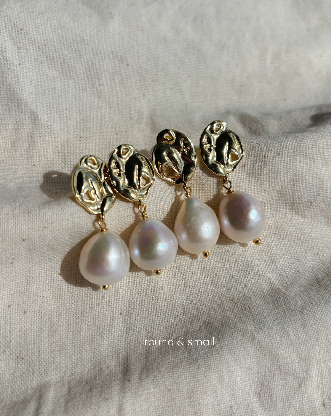 four round large pearl earrings are lyings aligned on a beige textile undrer a soft sunlight