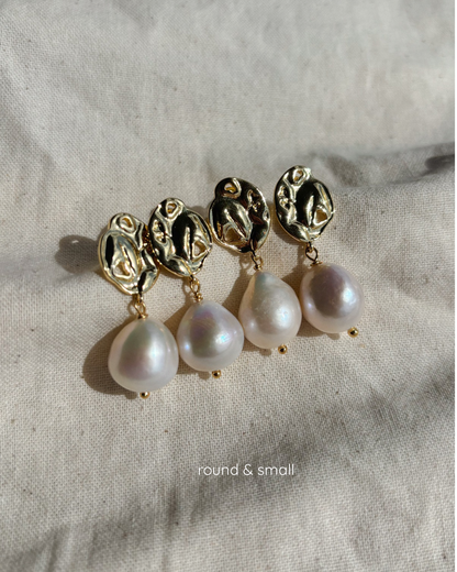 four round large pearl earrings are lyings aligned on a beige textile undrer a soft sunlight