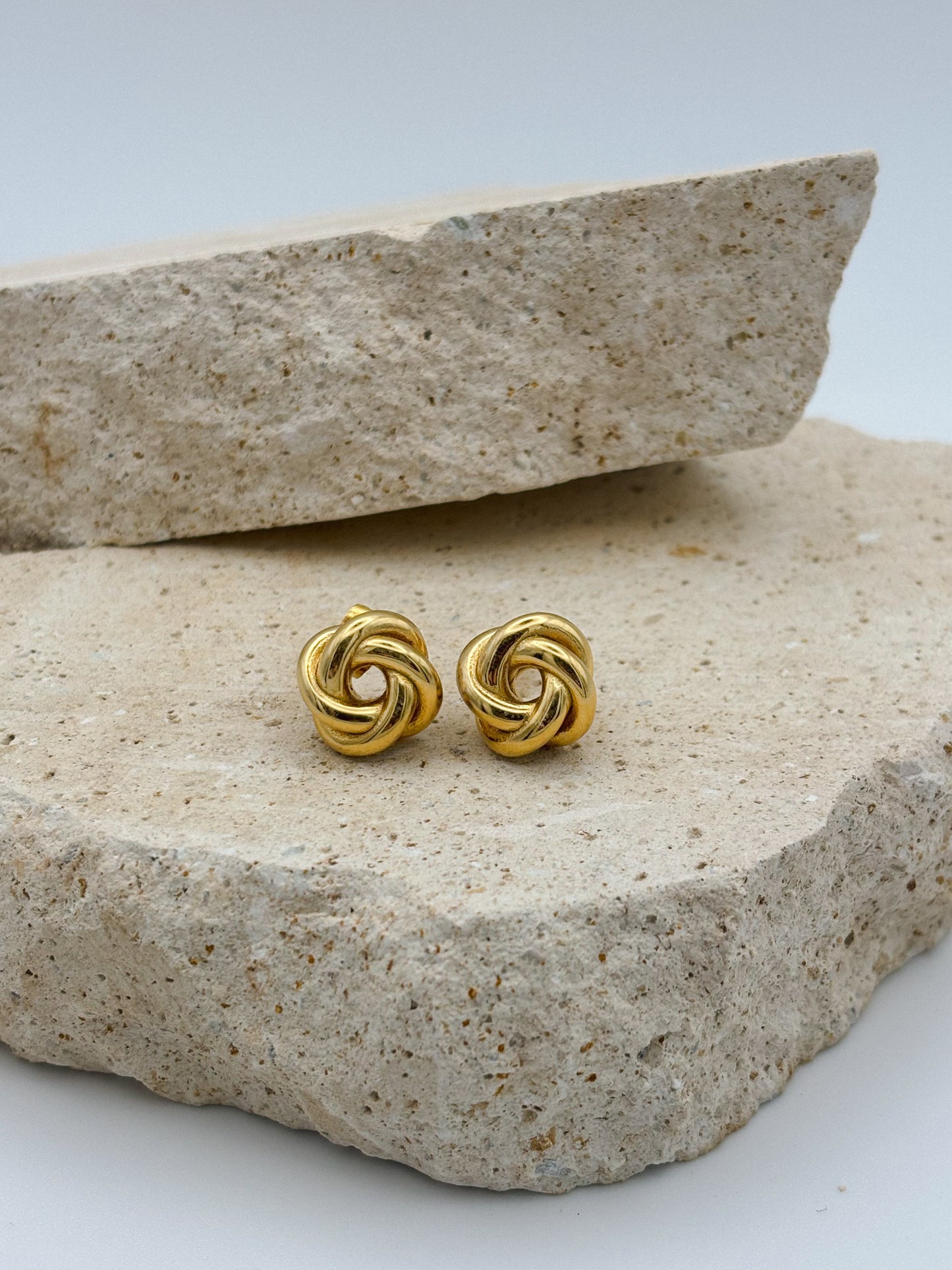 Gold knot stud earrings displayed on natural stone, minimalist and elegant jewelry design perfect for everyday or special occasions