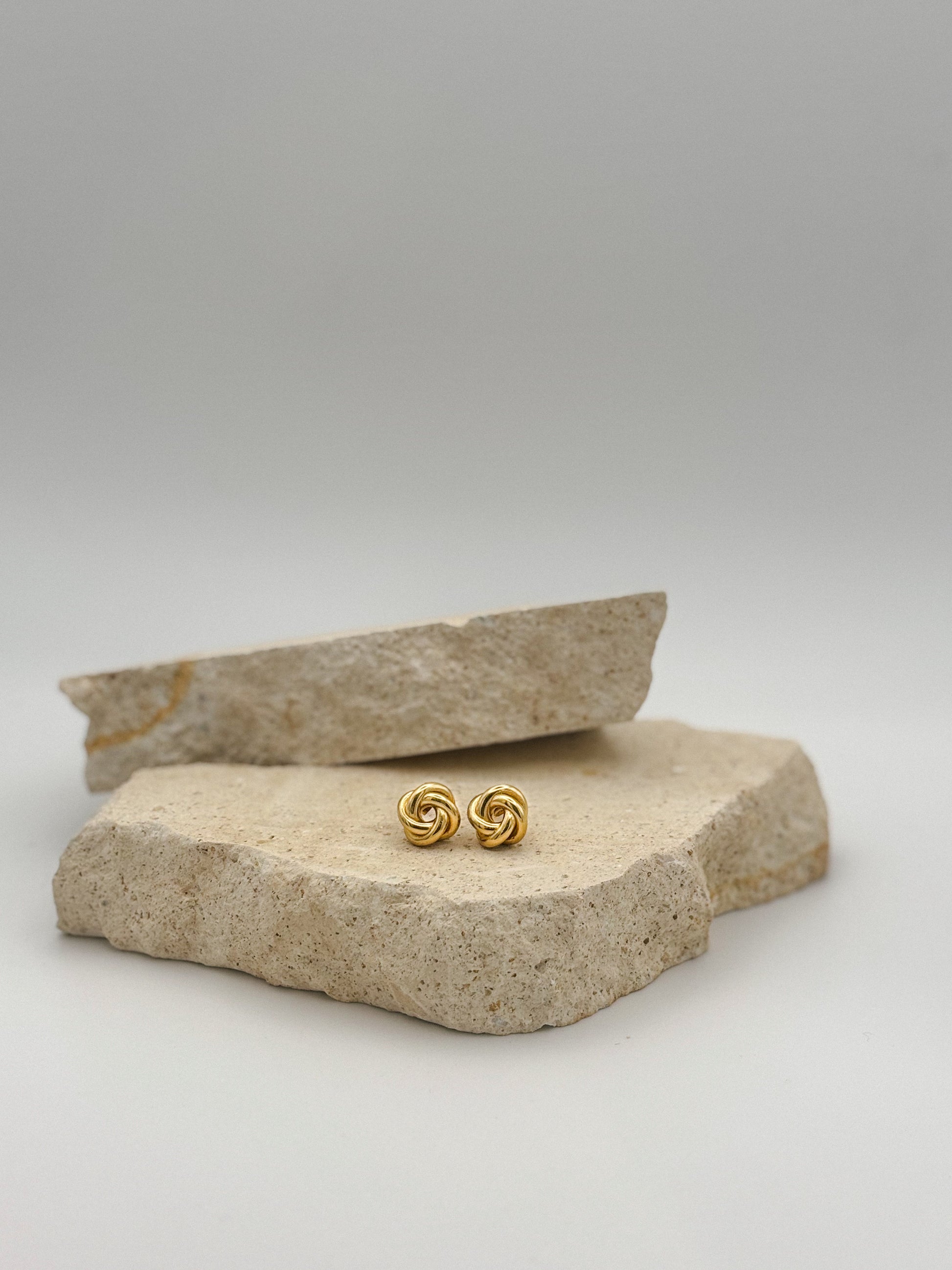 Gold knot stud earrings displayed on natural stone, minimalist and elegant jewelry design perfect for everyday or special occasions