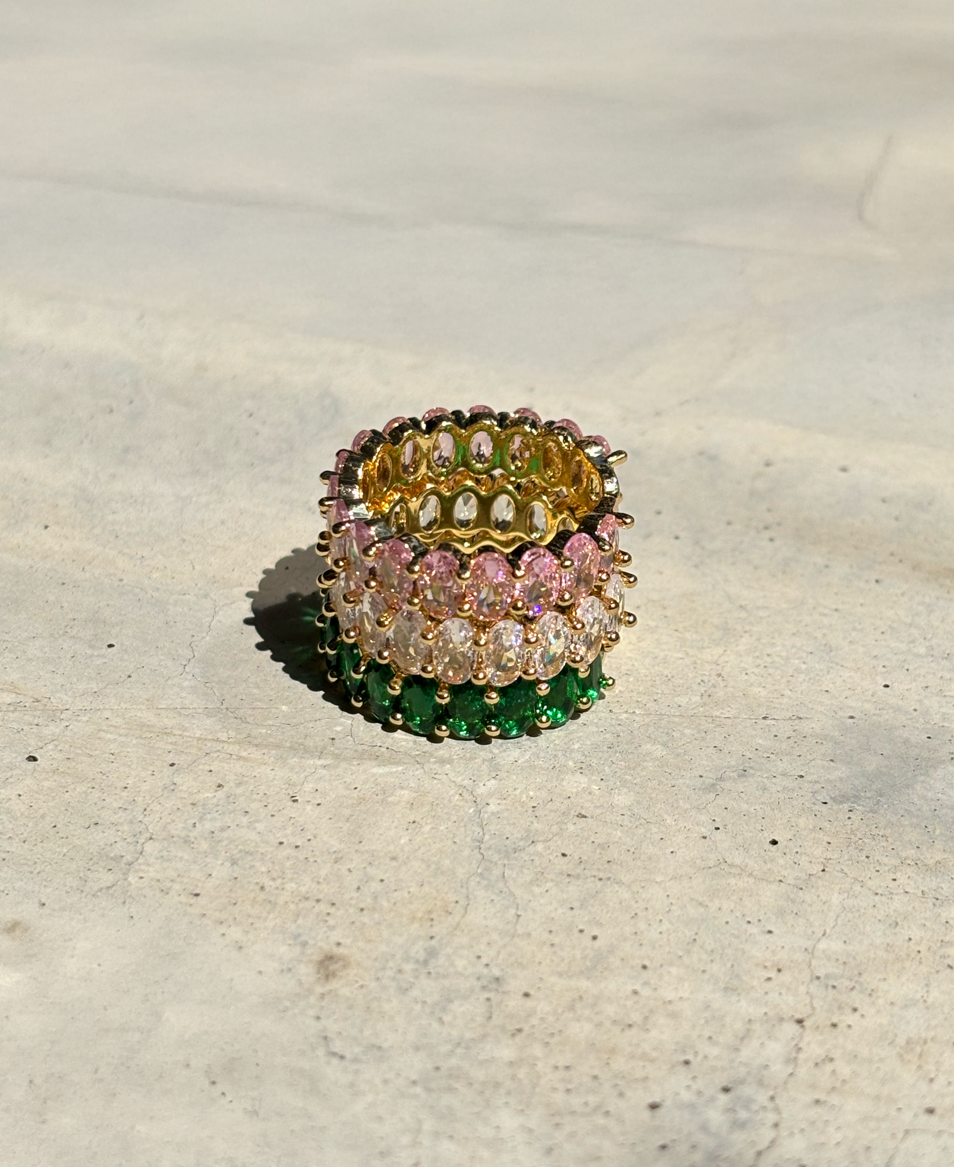 pink, clear and green zirconia stone rings are stacked on each other on a concrete plate with soft sunlight