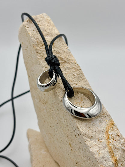Minimalist necklace with polished silver rings on a black adjustable cord, displayed on stacked natural stone — unisex modern jewelry with clean, sculptural design