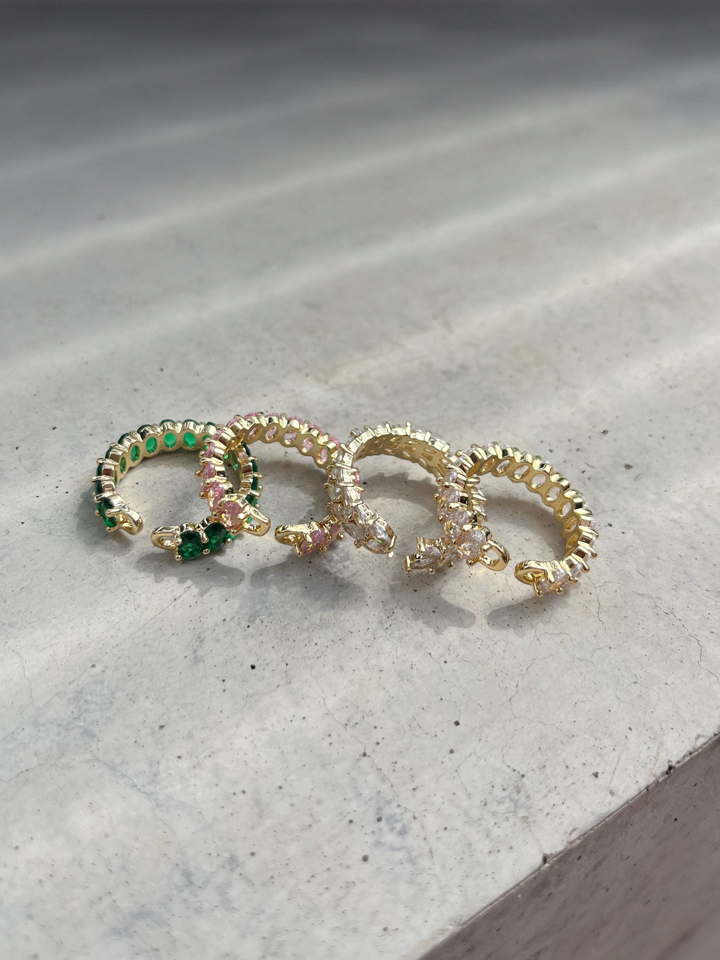 Four rings out of the shiny zirconia stones laying on a concrete plate, sunlight is soft